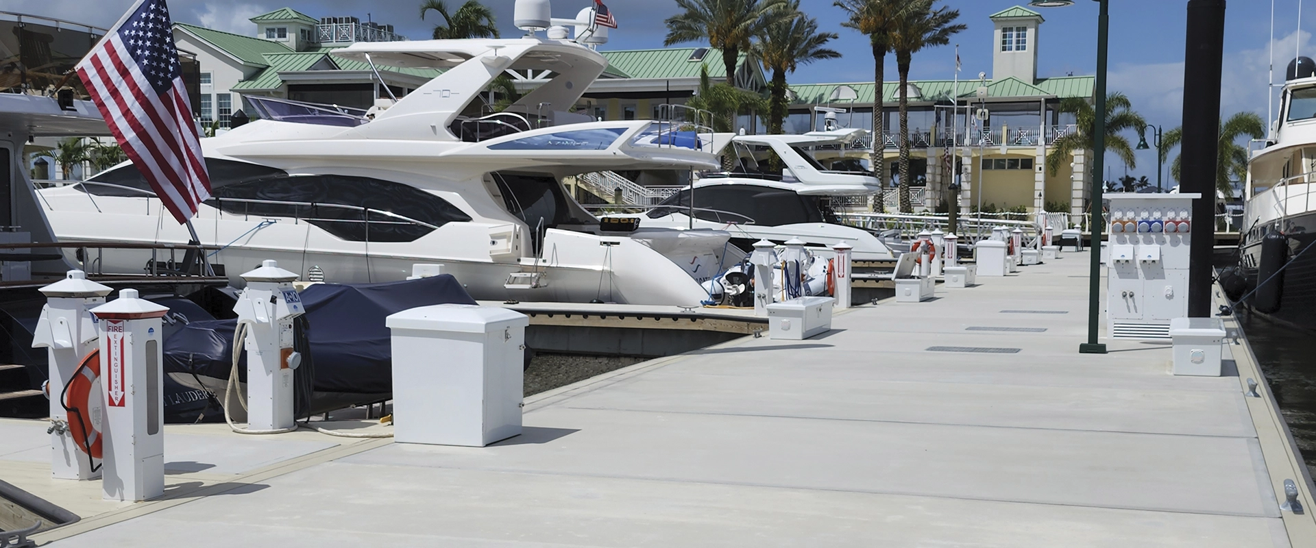 Marina with white yachts docked along a sunlit pier; an American flag flies from a boat