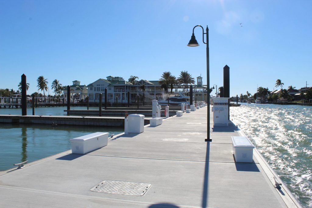 Dock along a sunny marina with boats, palm trees, and a lamppost in the foreground