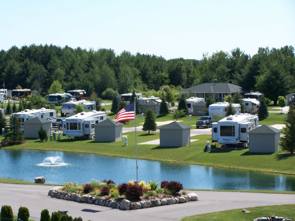 RV park along a lake with a fountain, American flag, and pine trees in the background